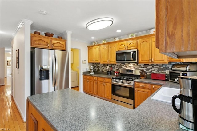 kitchen featuring appliances with stainless steel finishes, washer / dryer, sink, backsplash, and crown molding