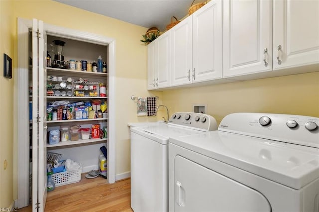 clothes washing area with washing machine and dryer, cabinets, and light wood-type flooring