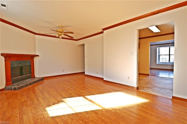 unfurnished living room featuring ceiling fan, ornamental molding, a tiled fireplace, and light wood-type flooring