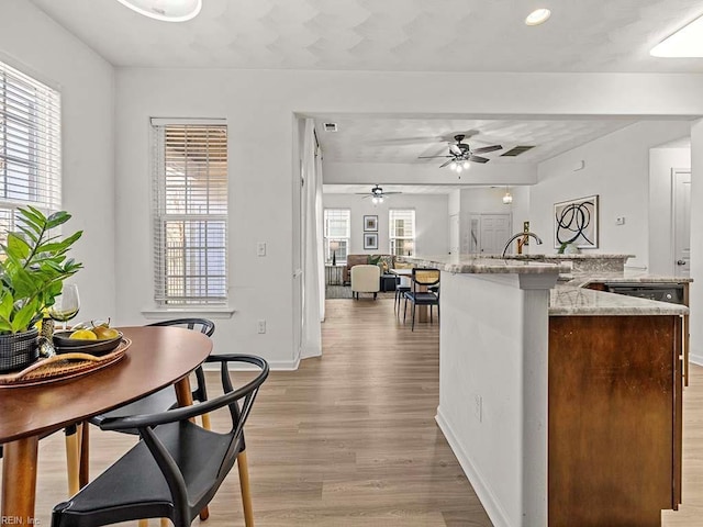 kitchen featuring sink, light stone counters, light wood-type flooring, ceiling fan, and a kitchen island with sink