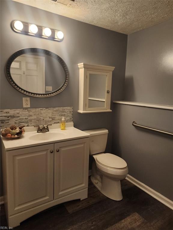 bathroom featuring hardwood / wood-style flooring, vanity, a textured ceiling, decorative backsplash, and toilet