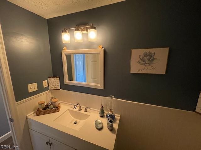 bathroom featuring vanity, a textured ceiling, and wainscoting