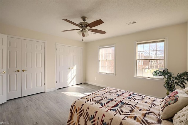 bedroom with ceiling fan, a textured ceiling, light hardwood / wood-style flooring, and multiple closets