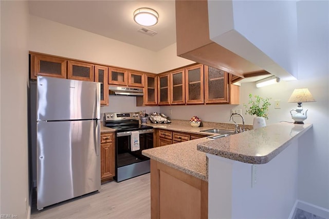 kitchen with appliances with stainless steel finishes, kitchen peninsula, sink, light hardwood / wood-style floors, and light stone counters