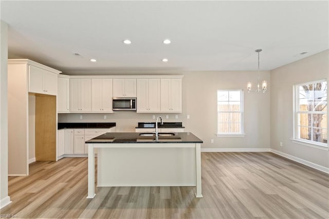 kitchen with sink, light hardwood / wood-style flooring, a kitchen island with sink, hanging light fixtures, and white cabinets