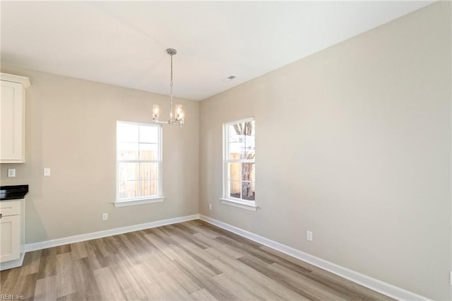 unfurnished dining area featuring an inviting chandelier and light hardwood / wood-style floors