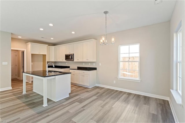 kitchen featuring sink, hanging light fixtures, a center island with sink, a kitchen breakfast bar, and white cabinets