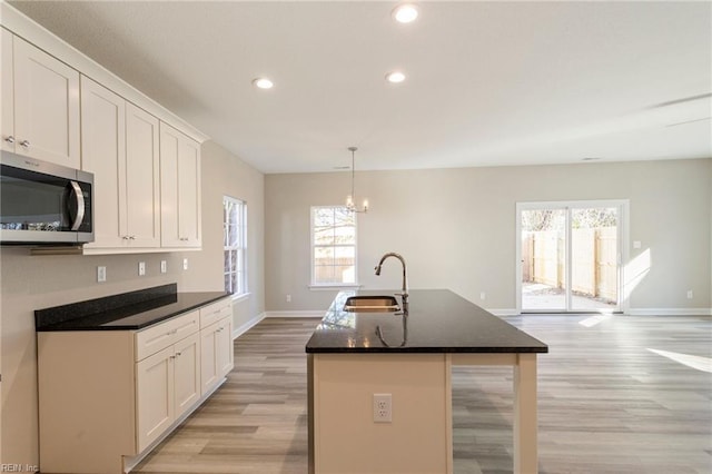 kitchen featuring white cabinetry, hanging light fixtures, sink, and a center island with sink