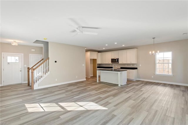 kitchen with ceiling fan with notable chandelier, pendant lighting, sink, white cabinets, and light wood-type flooring