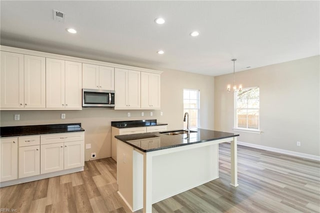 kitchen with sink, white cabinetry, an island with sink, pendant lighting, and light hardwood / wood-style floors