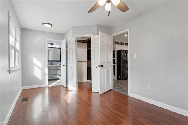 unfurnished bedroom with a walk in closet, wood-type flooring, and black fridge