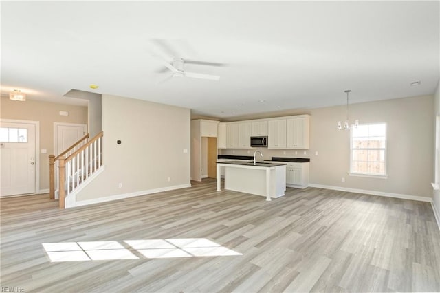 unfurnished living room with sink, ceiling fan with notable chandelier, and light hardwood / wood-style floors