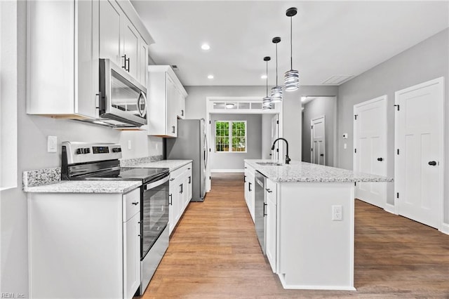 kitchen with white cabinetry, light stone counters, appliances with stainless steel finishes, pendant lighting, and a kitchen island with sink