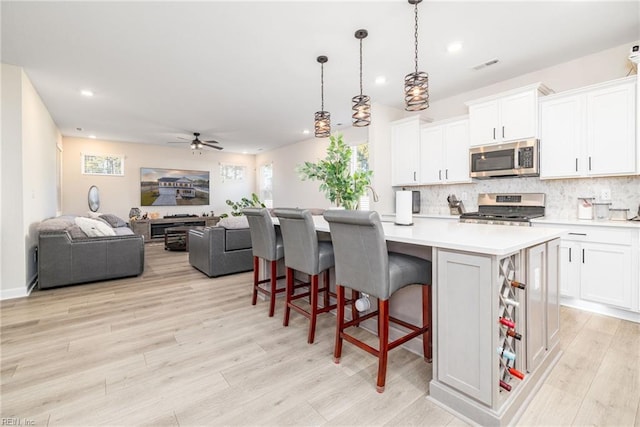 kitchen with appliances with stainless steel finishes, decorative light fixtures, white cabinets, a kitchen breakfast bar, and a center island with sink