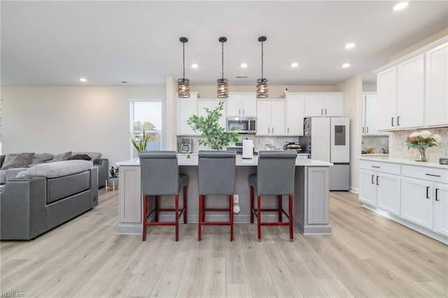 kitchen featuring a kitchen island with sink, pendant lighting, white cabinetry, and appliances with stainless steel finishes