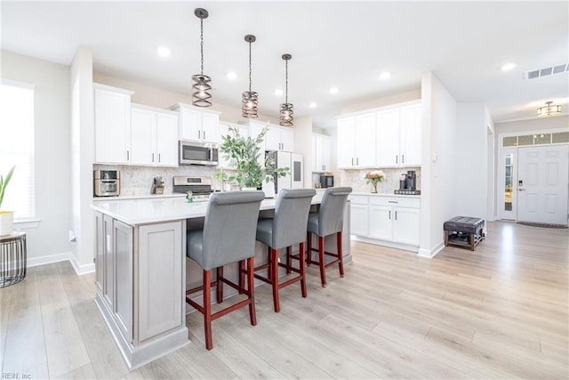 kitchen with appliances with stainless steel finishes, decorative light fixtures, an island with sink, and white cabinets