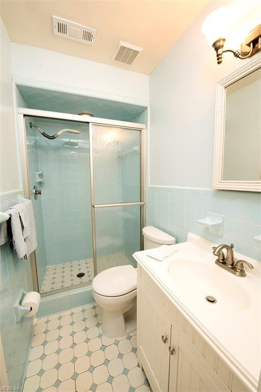 bathroom with vanity, a shower with shower door, tile walls, and toilet