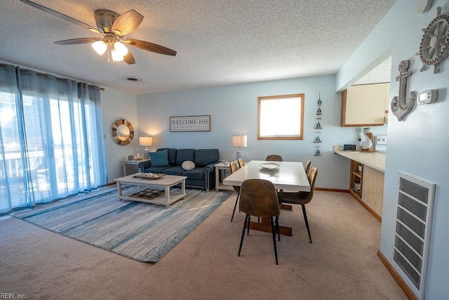 dining space featuring heating unit, ceiling fan, light colored carpet, and a textured ceiling