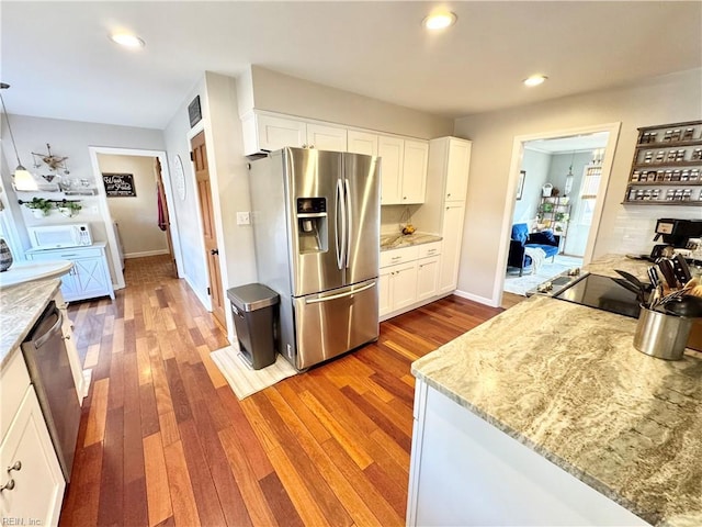 kitchen with pendant lighting, white cabinetry, hardwood / wood-style flooring, stainless steel appliances, and light stone countertops