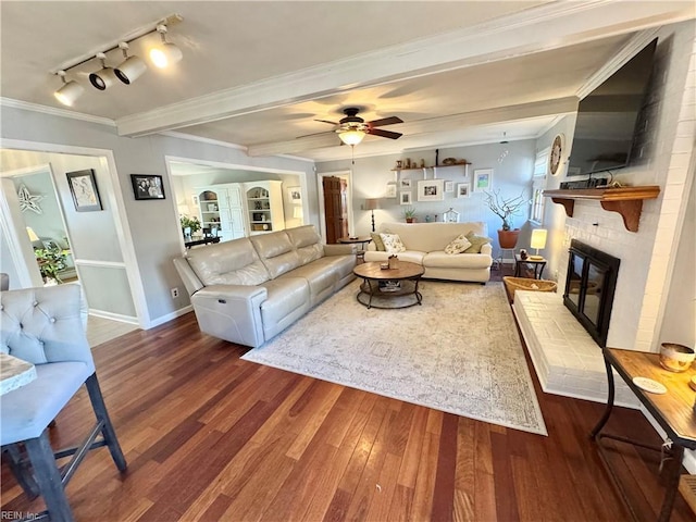 living room featuring dark hardwood / wood-style floors, ceiling fan, crown molding, a brick fireplace, and beam ceiling