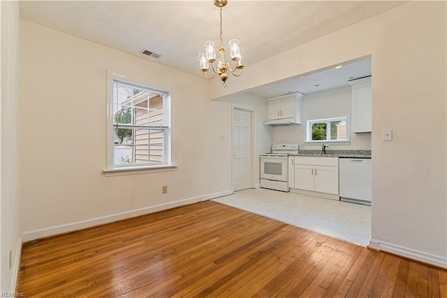 kitchen with white appliances, a chandelier, white cabinets, and light wood-type flooring