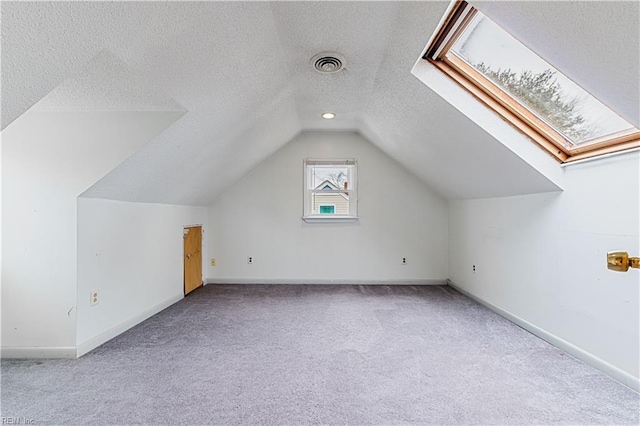 bonus room featuring light colored carpet, vaulted ceiling with skylight, and a textured ceiling