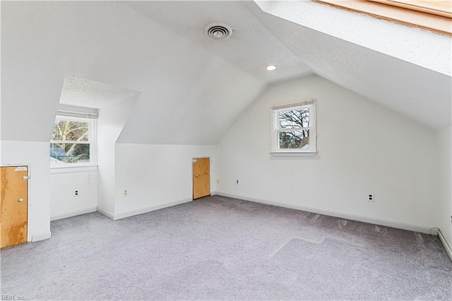 additional living space with vaulted ceiling, a wealth of natural light, light colored carpet, and a textured ceiling