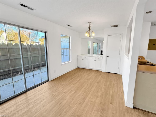 unfurnished dining area with sink, a wealth of natural light, a chandelier, and light wood-type flooring