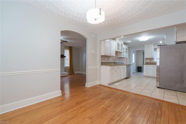 kitchen with hanging light fixtures, stainless steel appliances, light stone counters, white cabinets, and light wood-type flooring