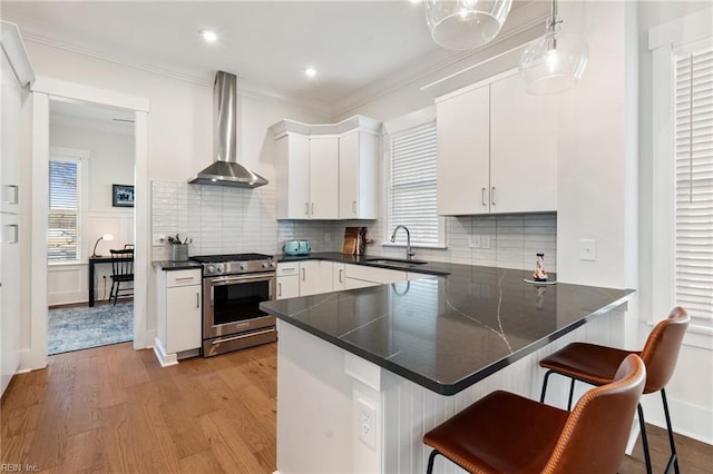 kitchen with wall chimney range hood, white cabinetry, decorative light fixtures, stainless steel range with gas cooktop, and kitchen peninsula