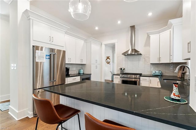 kitchen featuring pendant lighting, white cabinetry, high quality appliances, ornamental molding, and wall chimney exhaust hood