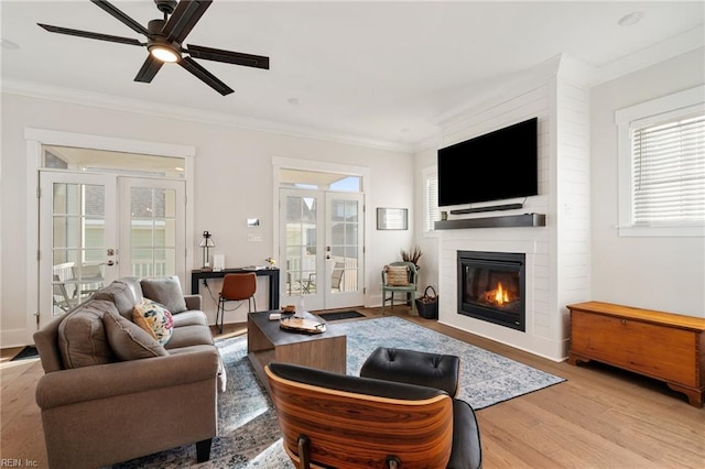 living room with french doors, a large fireplace, ornamental molding, and light hardwood / wood-style flooring