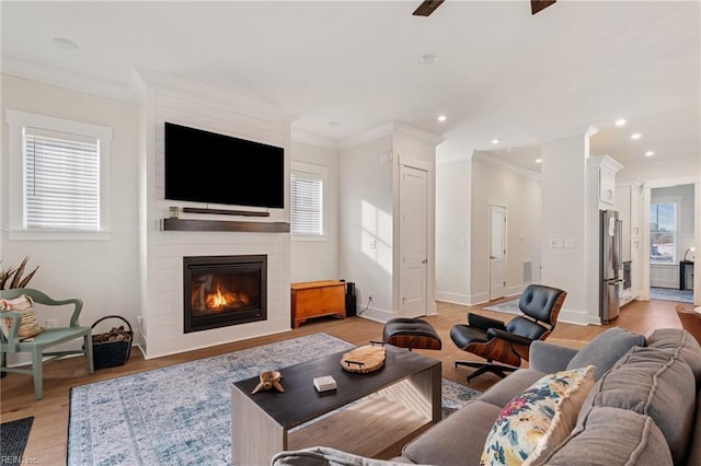 living room with ornamental molding, a fireplace, light hardwood / wood-style floors, and ceiling fan