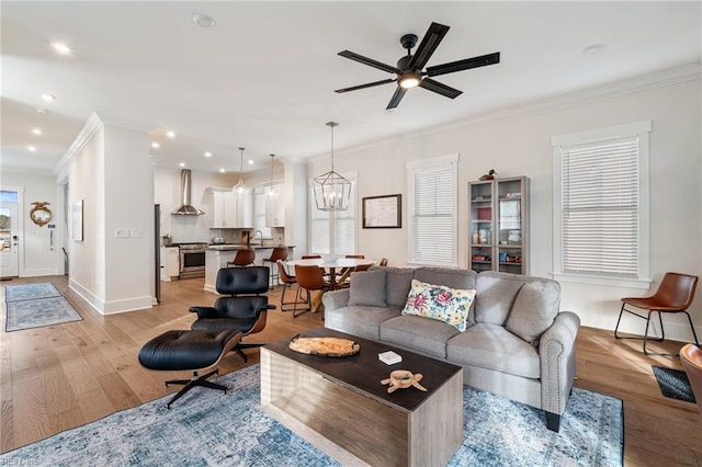 living room with ornamental molding, ceiling fan with notable chandelier, and light hardwood / wood-style floors