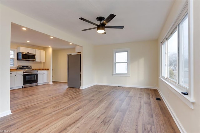 unfurnished living room with ceiling fan, a healthy amount of sunlight, and light wood-type flooring