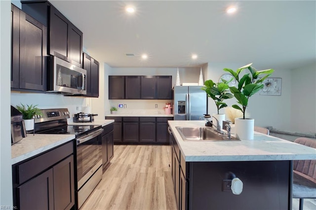 kitchen featuring a breakfast bar, sink, light wood-type flooring, appliances with stainless steel finishes, and a kitchen island with sink