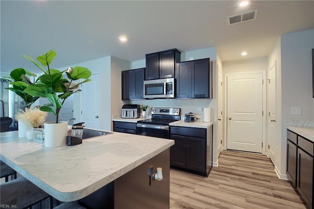 kitchen featuring stainless steel appliances, a breakfast bar area, a center island with sink, and light hardwood / wood-style flooring