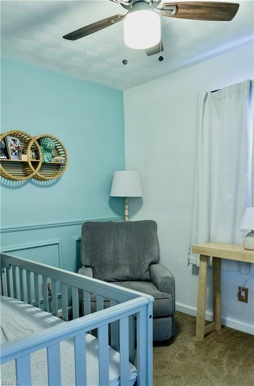 bedroom with a nursery area, light colored carpet, and ceiling fan