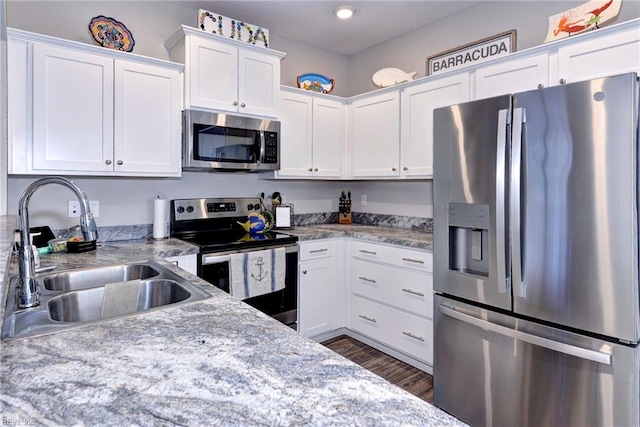 kitchen with sink, appliances with stainless steel finishes, white cabinetry, dark hardwood / wood-style floors, and light stone countertops