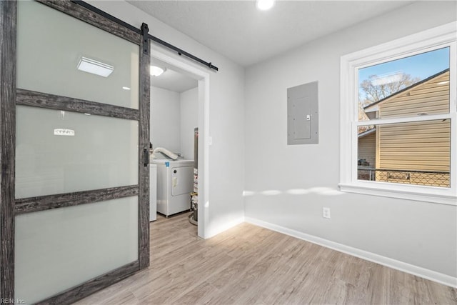 interior space with electric panel, a barn door, washer / dryer, and light hardwood / wood-style flooring