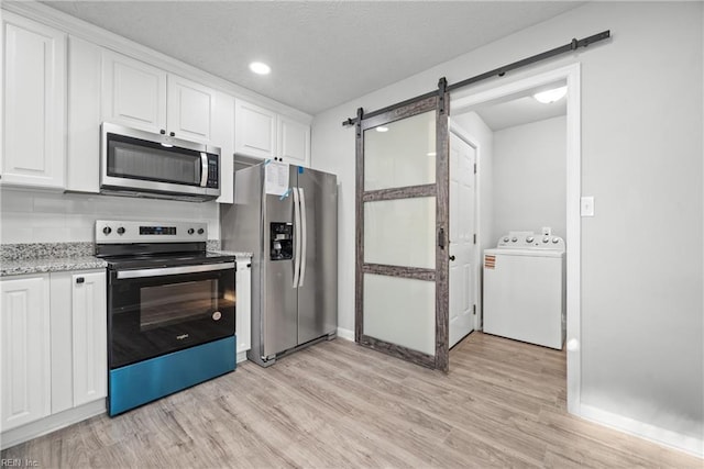 kitchen with washer / clothes dryer, white cabinetry, light hardwood / wood-style floors, stainless steel appliances, and a barn door