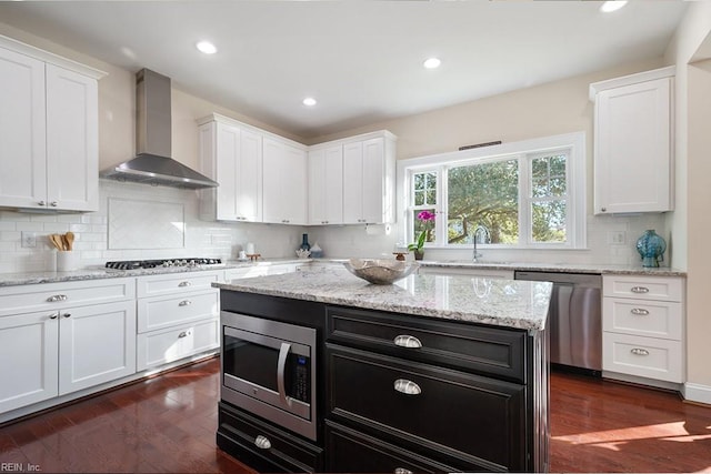 kitchen with a kitchen island, sink, white cabinets, stainless steel appliances, and wall chimney exhaust hood