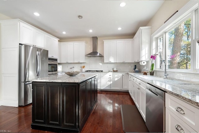 kitchen featuring light stone counters, appliances with stainless steel finishes, a center island, and wall chimney range hood