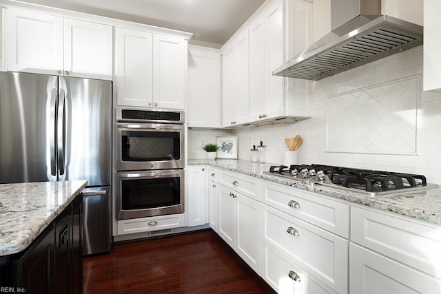 kitchen featuring wall chimney range hood, appliances with stainless steel finishes, light stone countertops, white cabinets, and dark hardwood / wood-style flooring