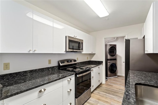 kitchen with white cabinetry, stacked washer / drying machine, stainless steel appliances, and dark stone countertops