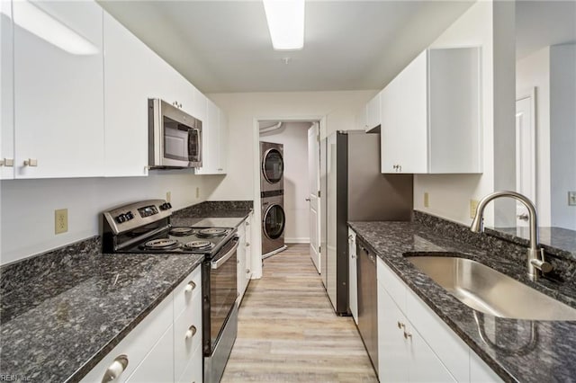 kitchen with sink, dark stone countertops, stainless steel appliances, stacked washer / dryer, and white cabinets