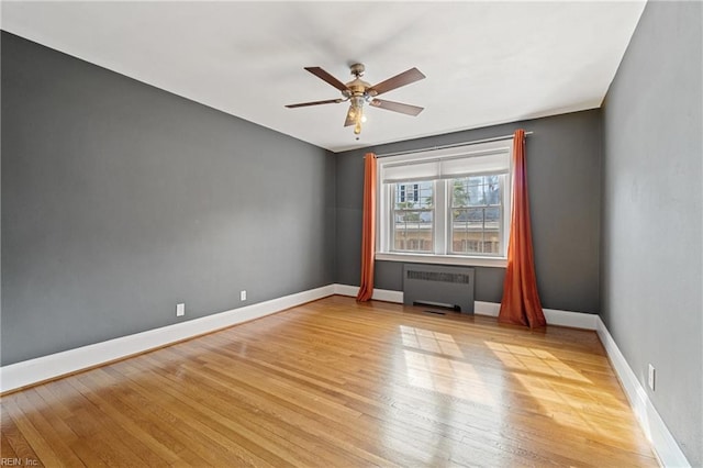 unfurnished room with ceiling fan, radiator heating unit, and light wood-type flooring