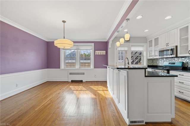 kitchen featuring hanging light fixtures, ornamental molding, appliances with stainless steel finishes, radiator, and white cabinets