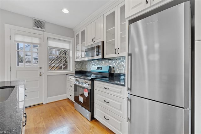 kitchen featuring appliances with stainless steel finishes, dark stone countertops, white cabinets, and backsplash