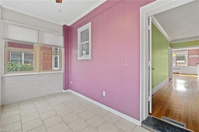 tiled empty room with brick wall, radiator heating unit, and ornamental molding